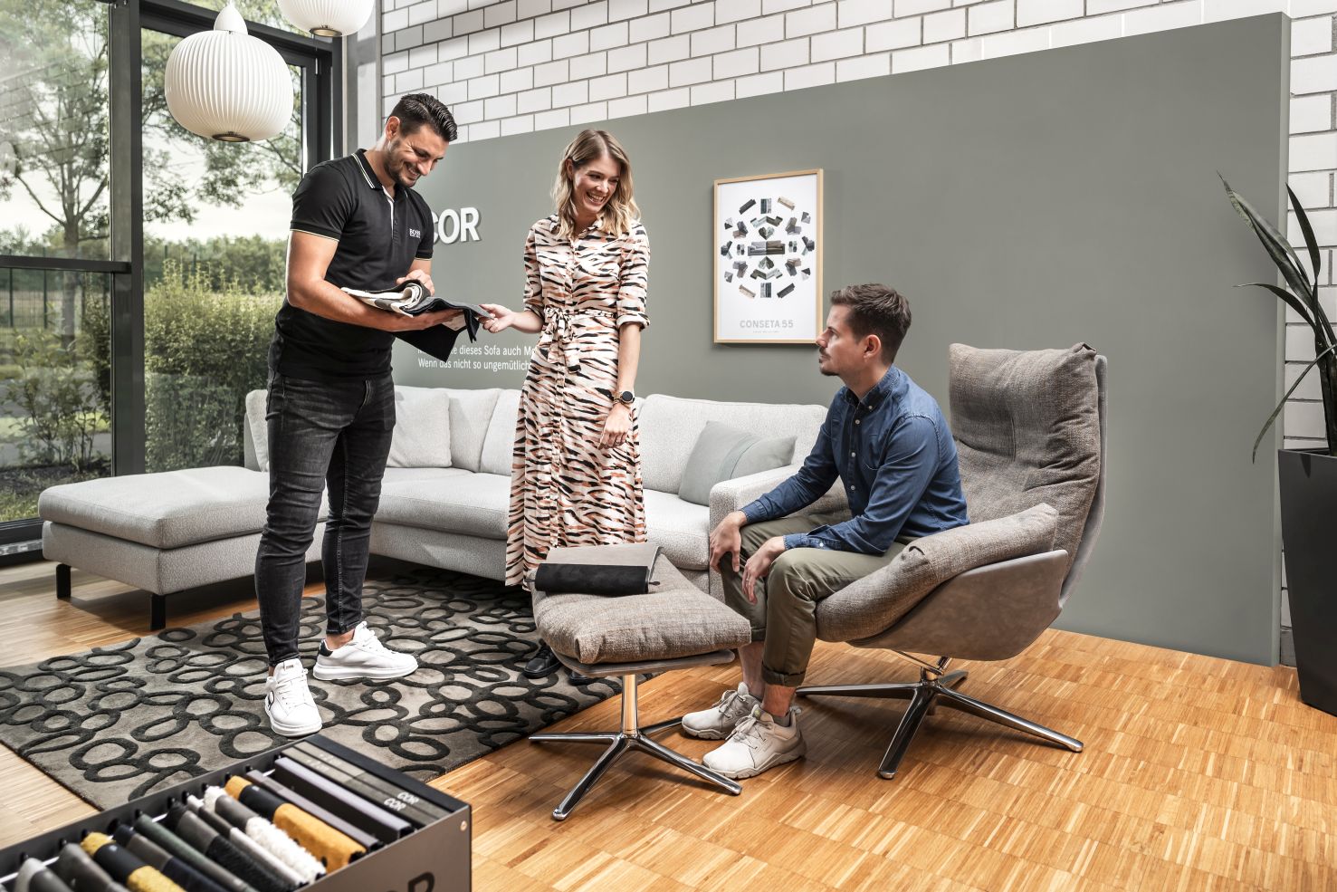 Beratungssituation in Design Möbel Ausstellung mit Sessel und Sofa sowie Materialmustern. 2 Kunden mit Berater von einrichten design.